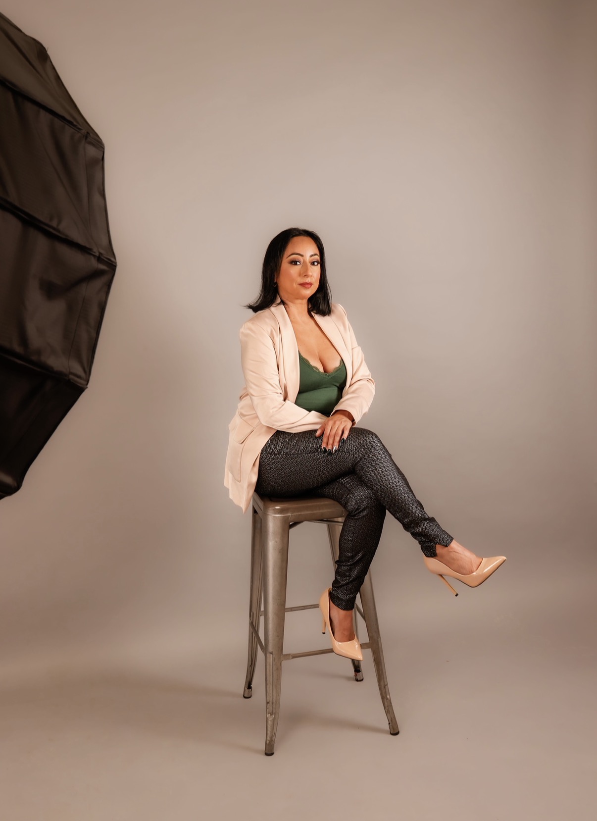 Angela seated on a studio stool wearing a pink blazer, green top, and patterned trousers